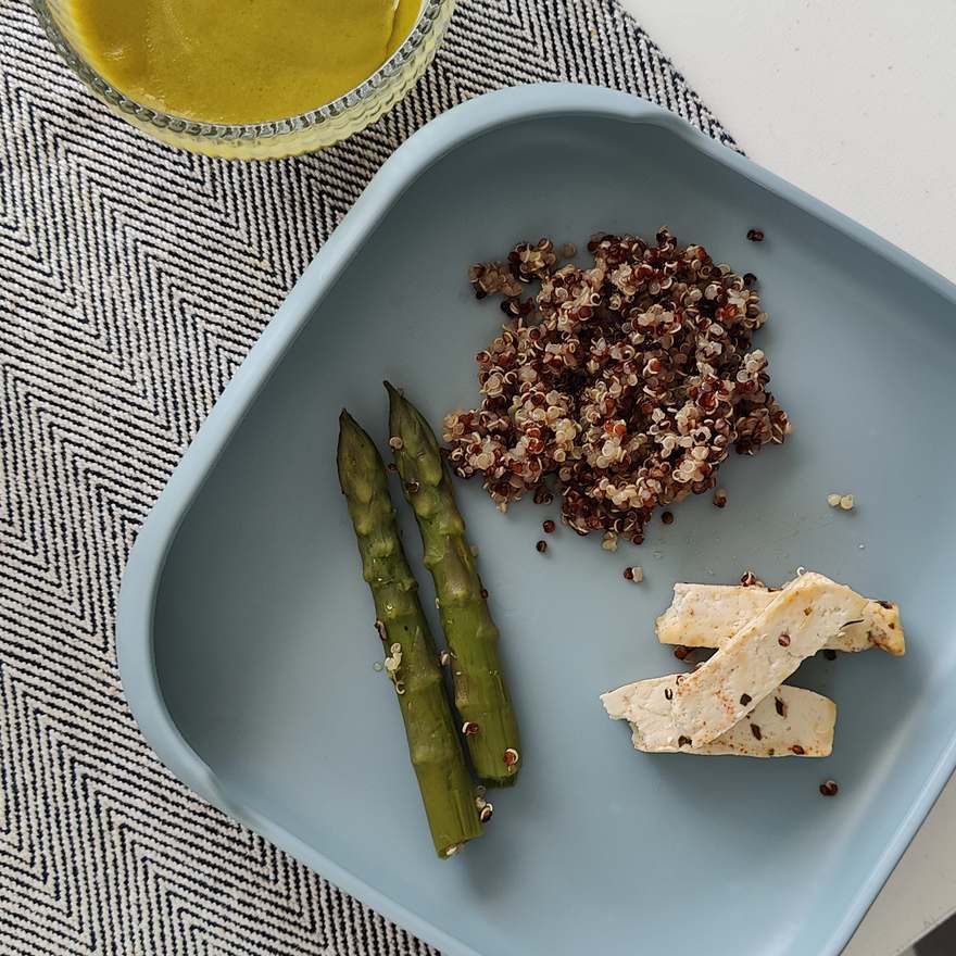 Prato azul com quinoa, espargos verdes e tiras de tofu sobre um pano de mesa